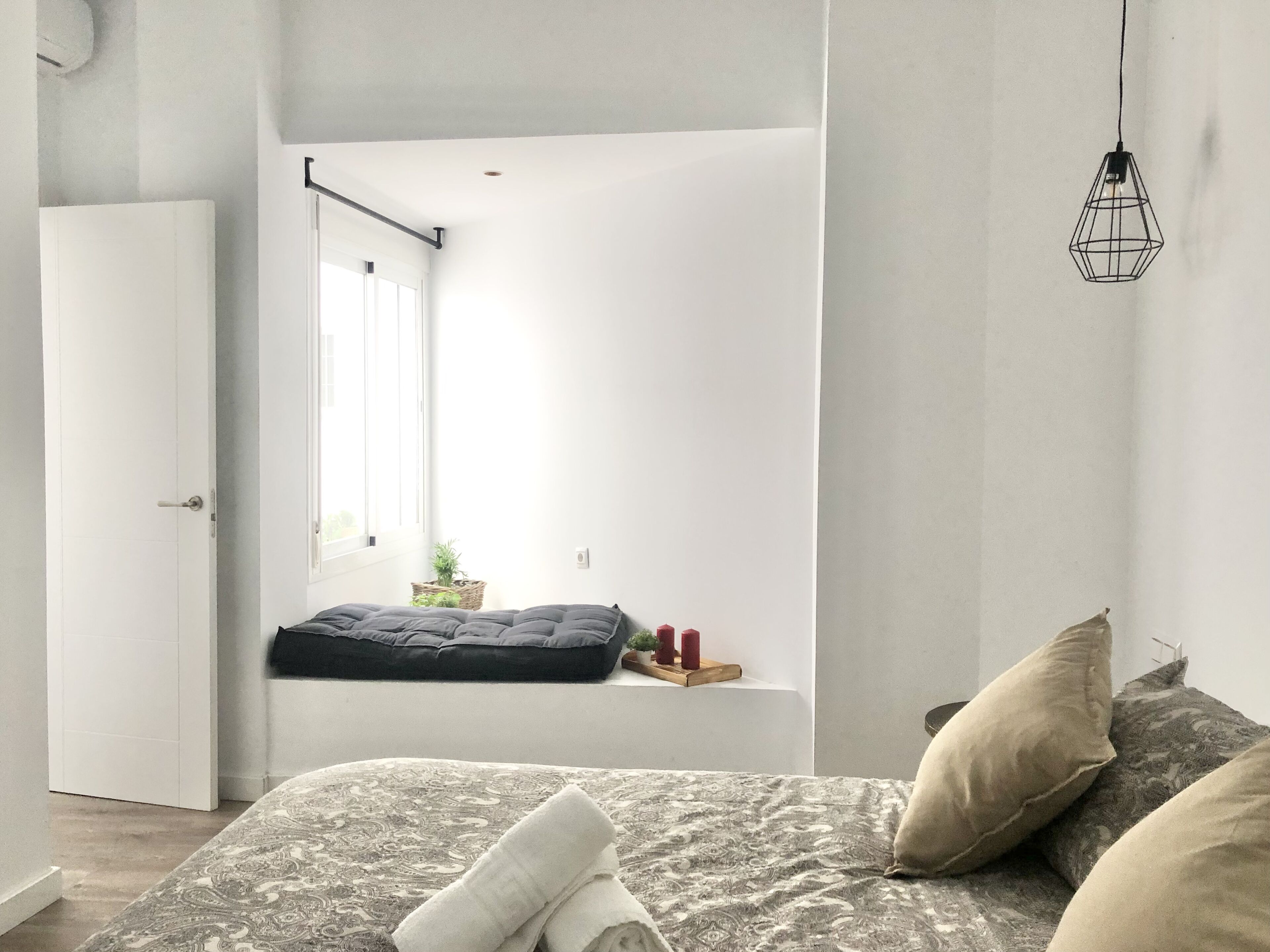 Un dormitorio con cama, ventana, estante con velas y lámpara colgante.