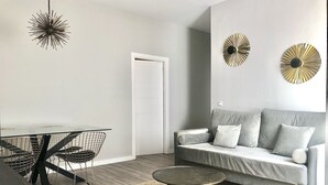 Una sala de estar moderna con un sofá gris, una mesa redonda de centro, una mesa de comedor con sillas y dos adornos colgantes en la pared.