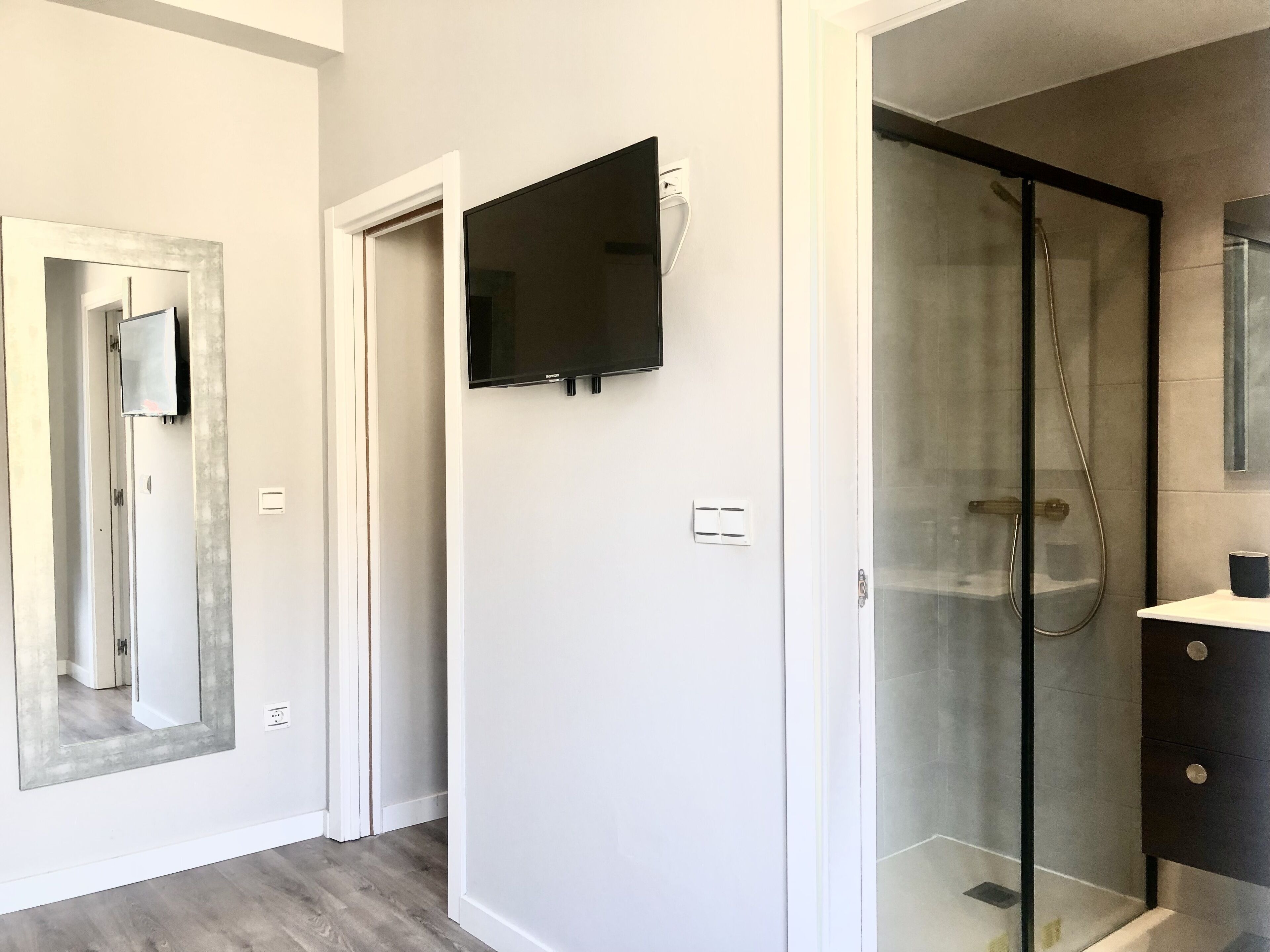 A modern bathroom with a glass shower enclosure, a mounted TV, and a large mirror.