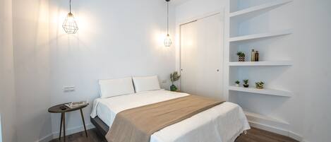 A modern bedroom with a bed, bedside tables, a ceiling fan, and built-in shelving with decorative items.