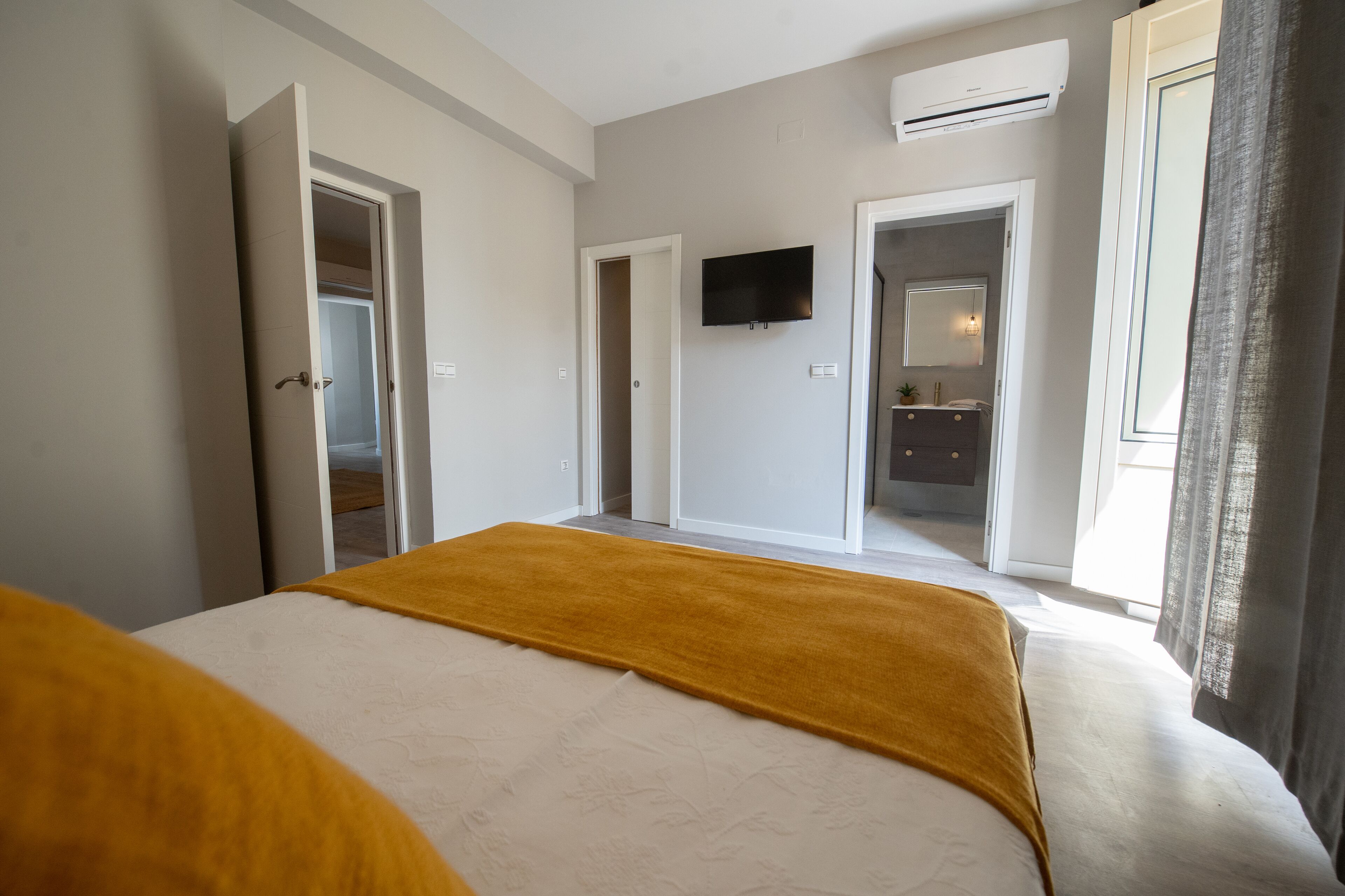 A hotel room with a bed, a television mounted on the wall, and a bathroom visible through an open door.