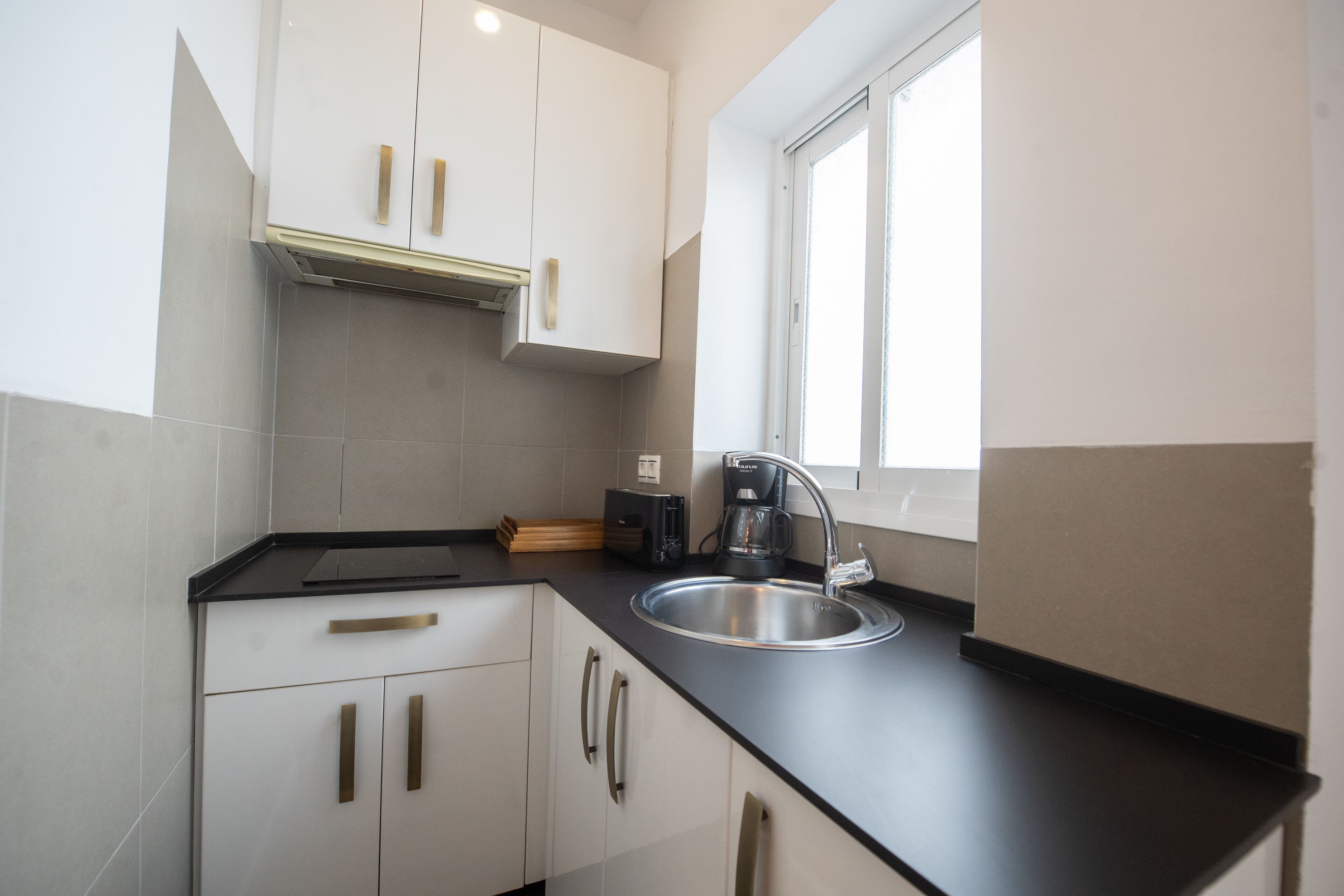 Cocina moderna con armarios blancos, encimera negra y pileta de acero inoxidable.