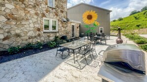 Ein Steinhaus mit einem großen Sonnenblumengemälde, Sitzgelegenheiten im Freien und einem Grill.