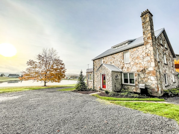 A stone house with a red door, a chimney, and a gravel driveway.