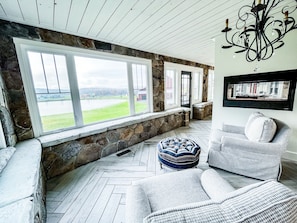 A cozy room with stone walls, large windows, and a chandelier.