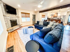 A modern living room with a fireplace, a large sofa set, and a kitchen in the background.
