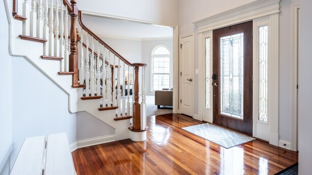 Un vestíbulo amplio con una escalera de madera, una puerta grande con paneles de vidrio y un ventanal luminoso.