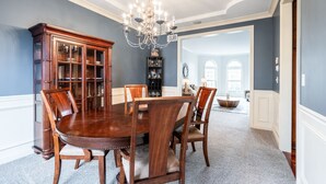 Un comedor con una mesa y sillas de madera, una araña y una estantería.