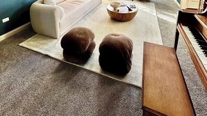 Una sala de estar con un sofá modular, dos sillones, una mesa de centro, otomanas, un piano y ventanas amplias con arcos.