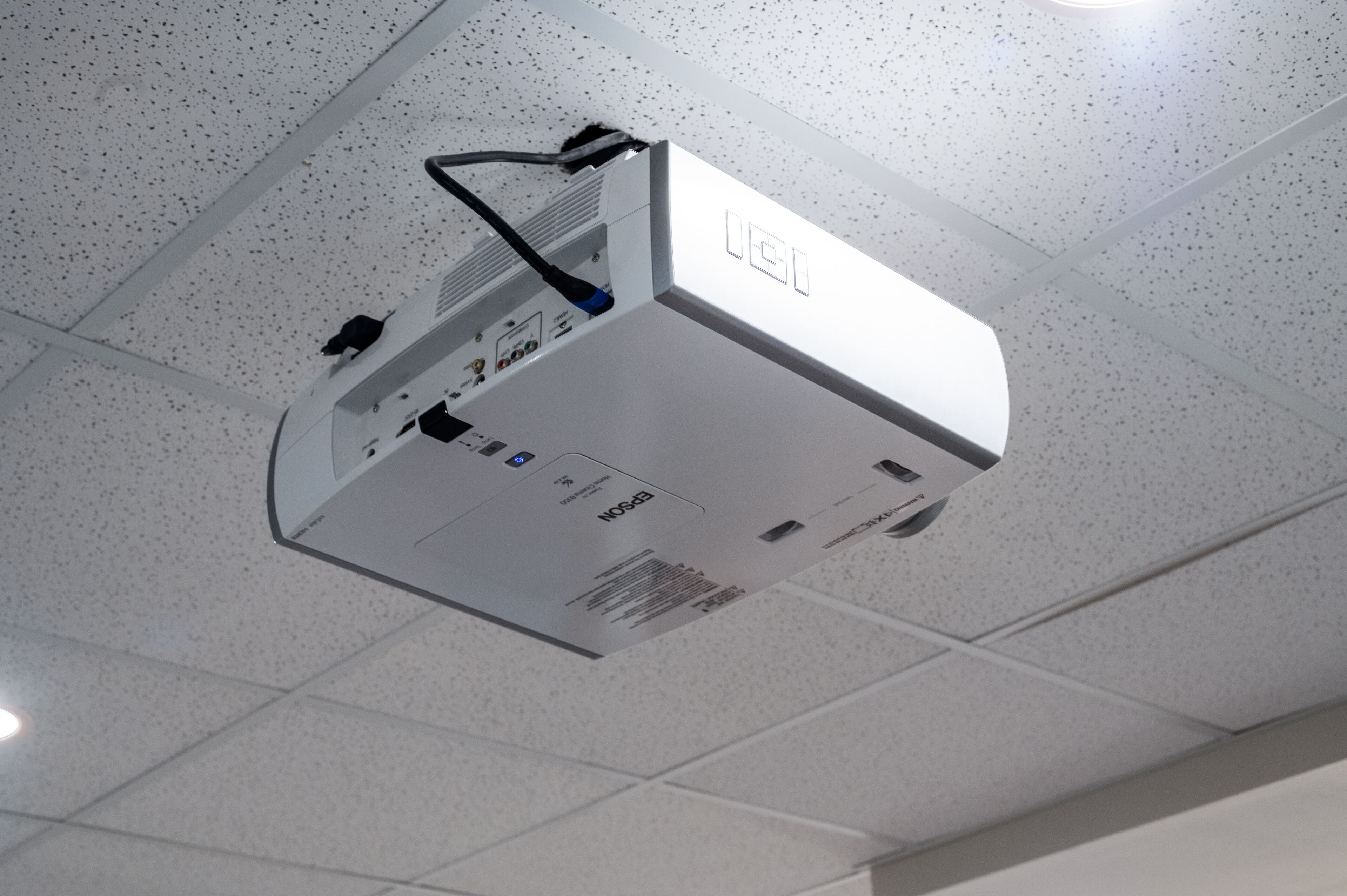 A ceiling-mounted projector with a control panel and a cable.