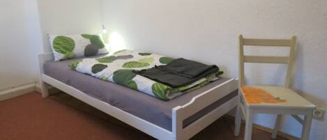 Una habitación pequeña con una cama individual, una silla de madera y una mesita de noche.