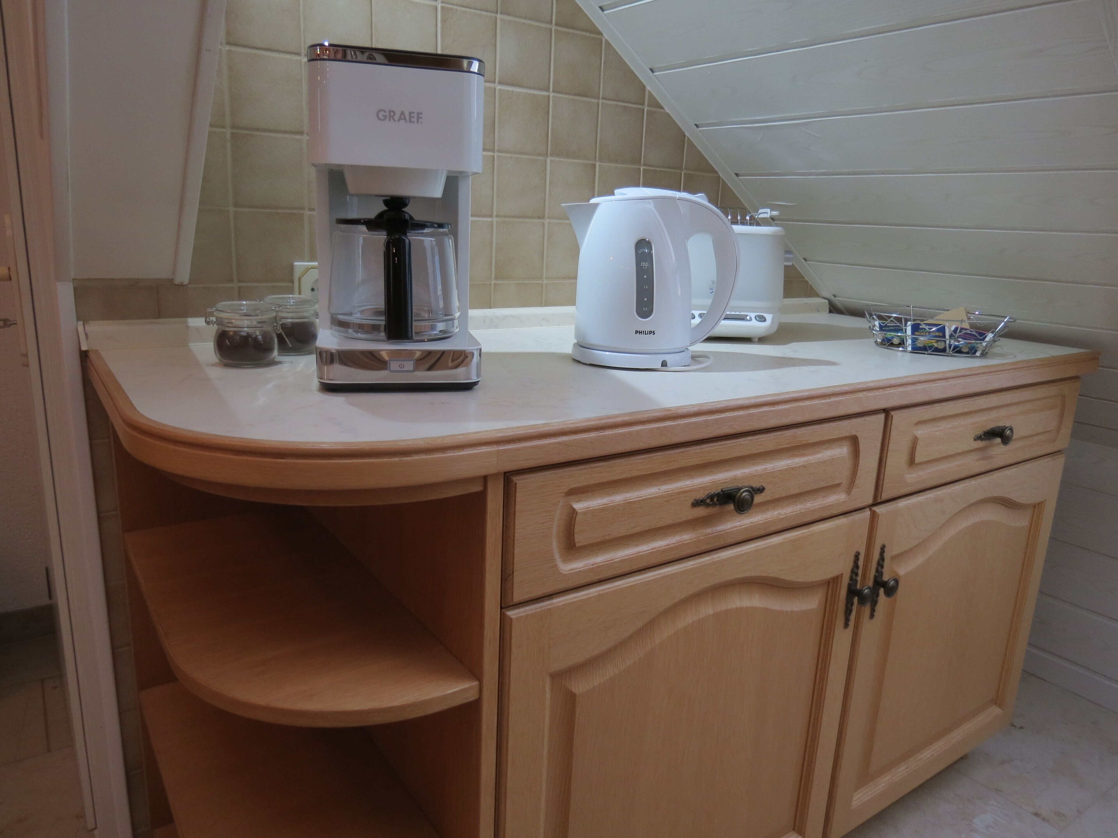 Una cocina con cafetera, hervidor y una cesta sobre la encimera.