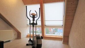 Une pièce dotée d’un ventilateur de plafond, d’un appareil d’exercice et d’une fenêtre donnant sur des immeubles.