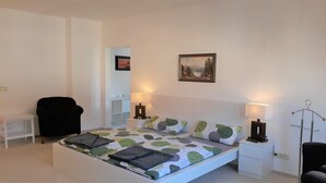Une chambre à coucher comprenant un lit, deux tables de chevet, une chaise, un bureau et une lampe fixée au mur.