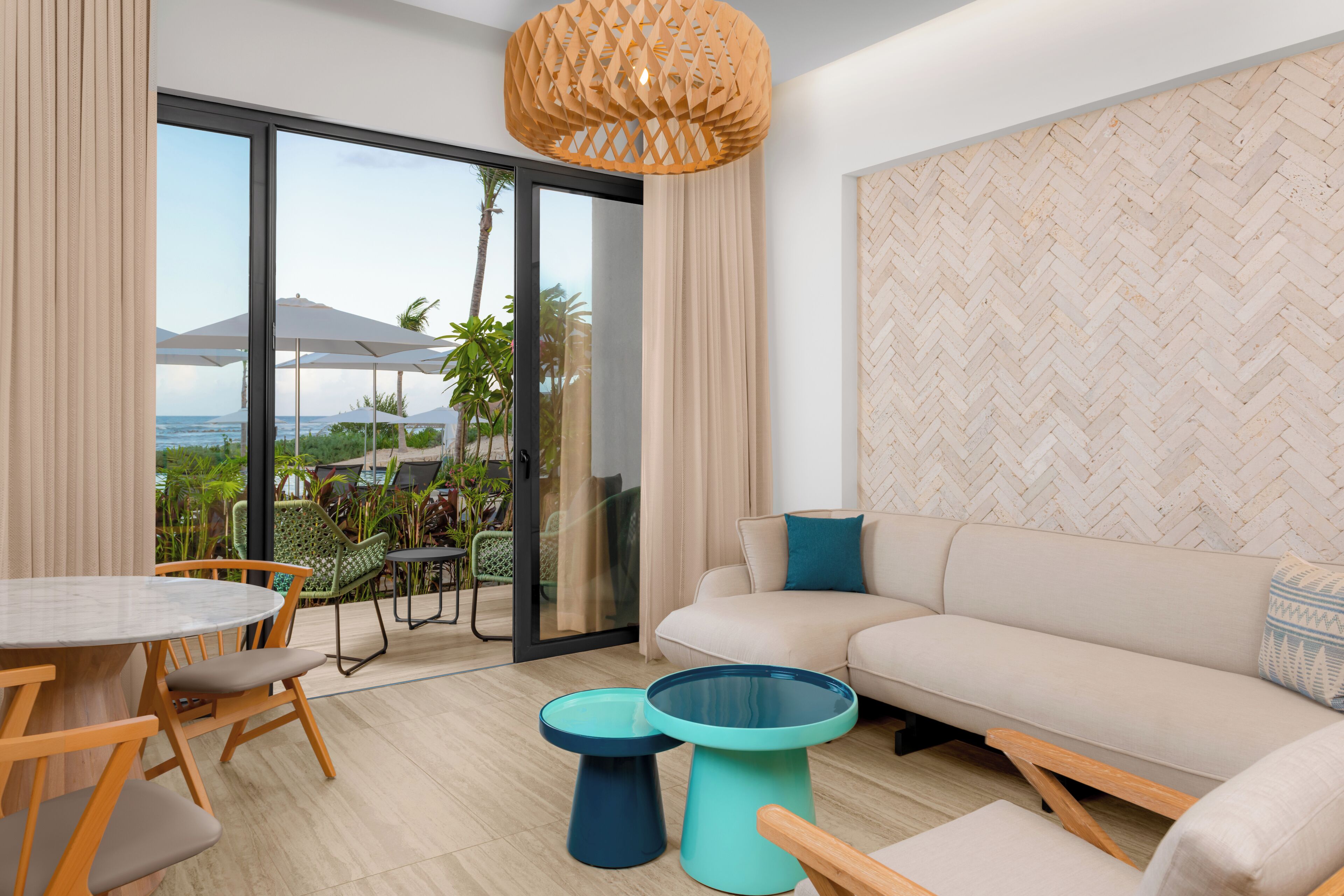 Uma sala de estar moderna com um sofá, duas mesas laterais, uma mesa de jantar com cadeiras e vista para o exterior.