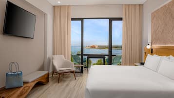 Ein Hotelzimmer mit einem großen Bett, einem Fernseher, Blick auf den Ozean und einem Balkon mit Tisch und Stühlen.