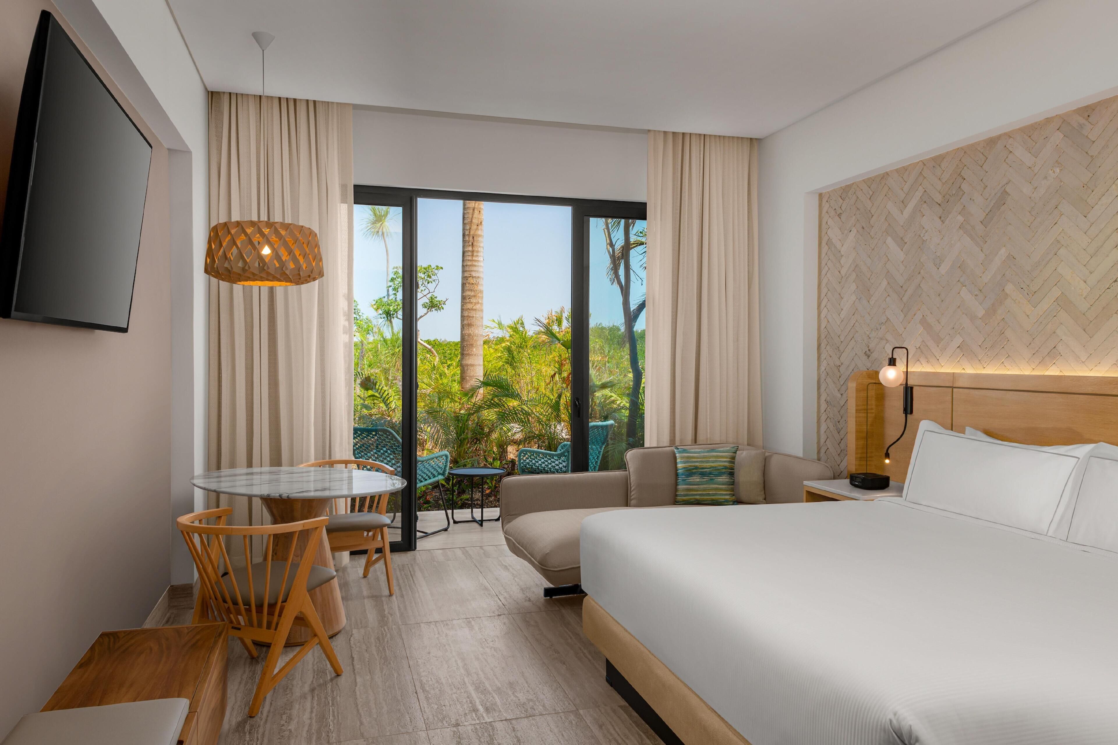 A hotel room with a large bed, a dining area with chairs, a sofa, and a TV mounted on the wall.