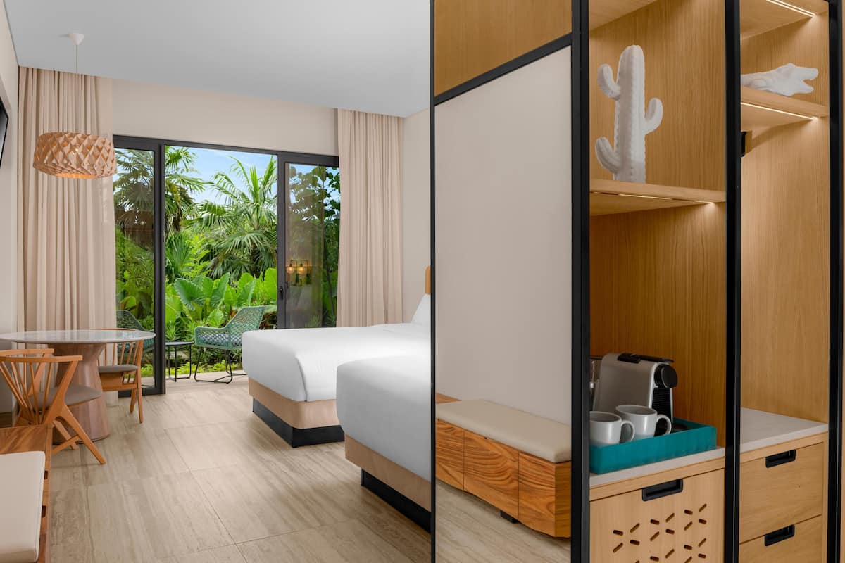A hotel room with a bed, a desk, and a view of greenery outside.