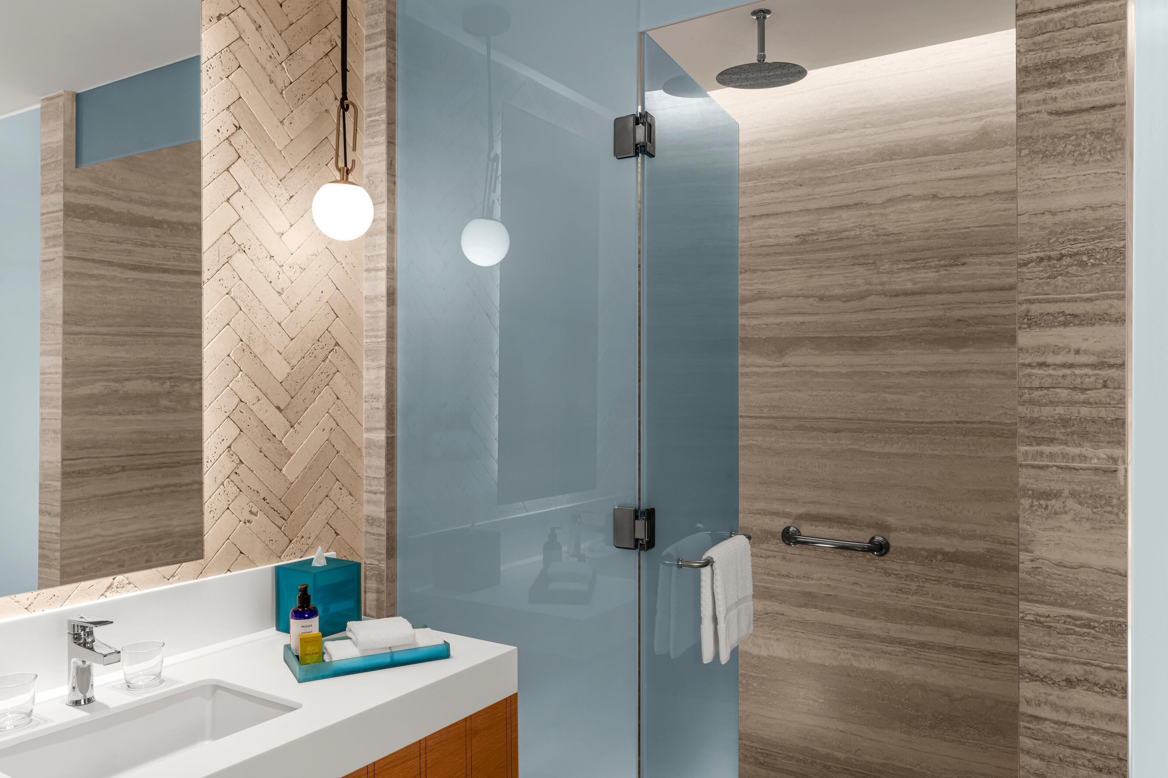 Un bagno moderno con box doccia in vetro, lavabo bianco e parete con motivo a spina di pesce.
