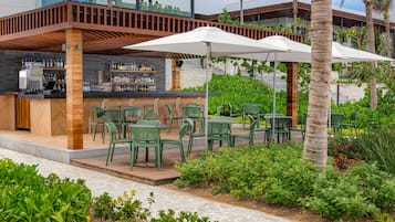 An outdoor bar area with green chairs and umbrellas, surrounded by lush greenery and palm trees.
