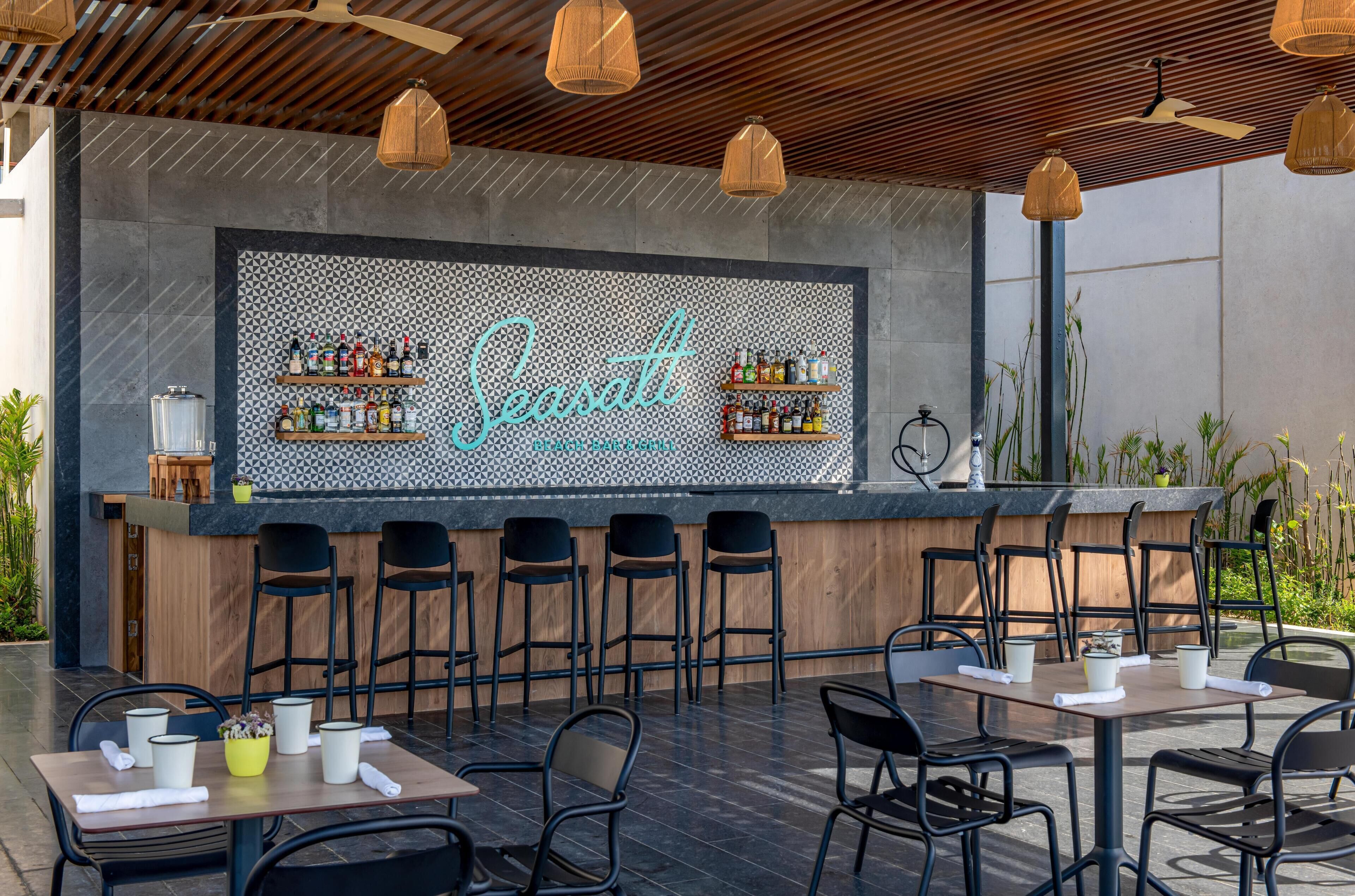 An outdoor bar area with a tiled backsplash, bar stools, and tables with chairs.