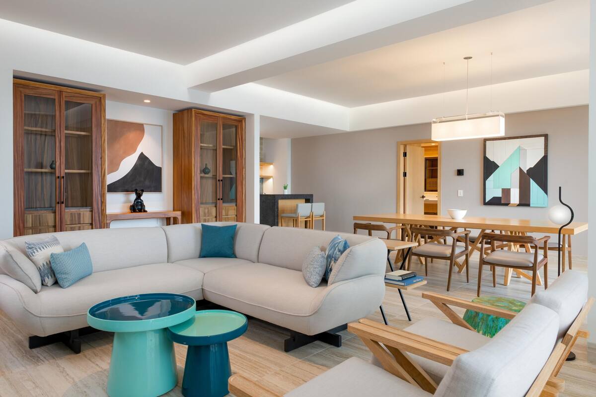 A modern living room with a sectional sofa, a dining area with wooden chairs, and a kitchen in the background.