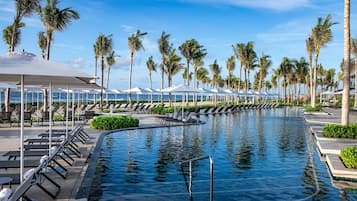 A poolside area with lounge chairs and umbrellas, surrounded by palm trees.