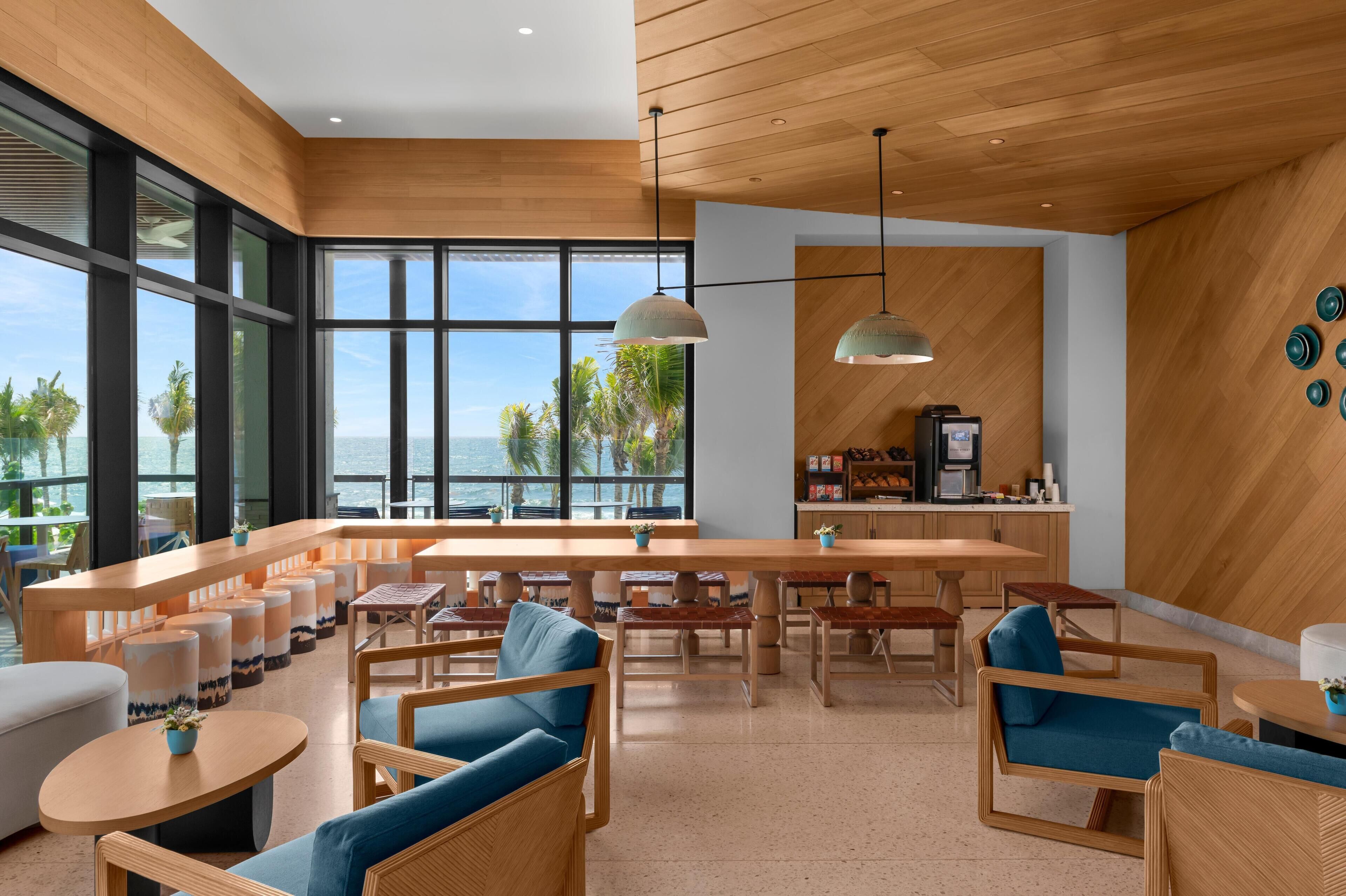 A modern lounge area with wooden furniture, a bar, and large windows offering a view of the ocean.
