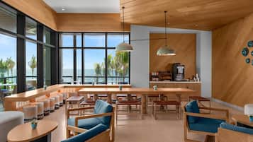 A modern lounge area with wooden furniture, a bar, and large windows offering a view of the ocean.