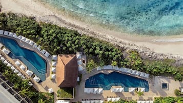 Vista aérea de un resort con dos piscinas, una playa y abundante vegetación.