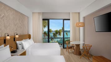 Une chambre d’hôtel avec deux lits, une télévision, un balcon donnant sur l’océan et un coin repas avec une table et des chaises.