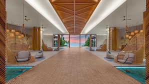 A modern hotel lobby with a long corridor, hanging chairs, and a view of the ocean.