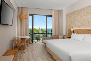 A hotel room with a large bed, a dining area with a table and chairs, a TV mounted on the wall, and a view of the ocean through large windows. - Hilton Tulum Riviera Maya All-Inclusive Resort (Tulum)