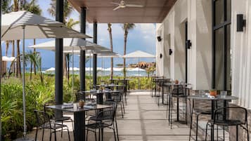 An outdoor patio with tables and chairs, umbrellas, and a view of the ocean.