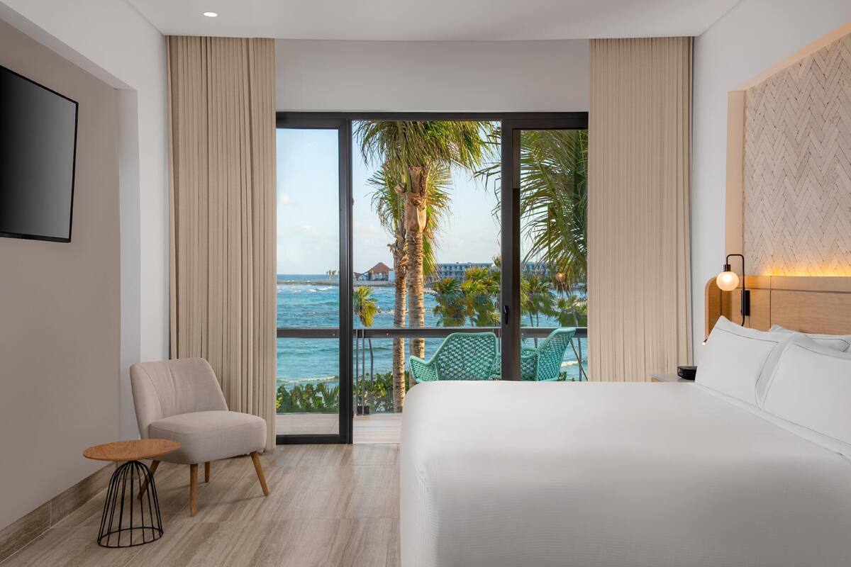 A hotel room with a large bed, a chair, a small table, and a view of the ocean.