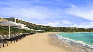 Di pantai, pasir putih, kursi berjemur, dan payung pantai
