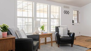 A living room with a black leather sofa, a wooden side table, a black leather armchair, and a large window with a view of trees.