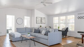 A spacious living room with a grey sofa, a coffee table, and a ceiling fan.