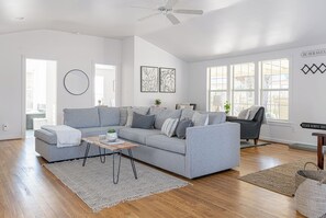 A spacious living room with a grey sofa, a coffee table, and a ceiling fan.