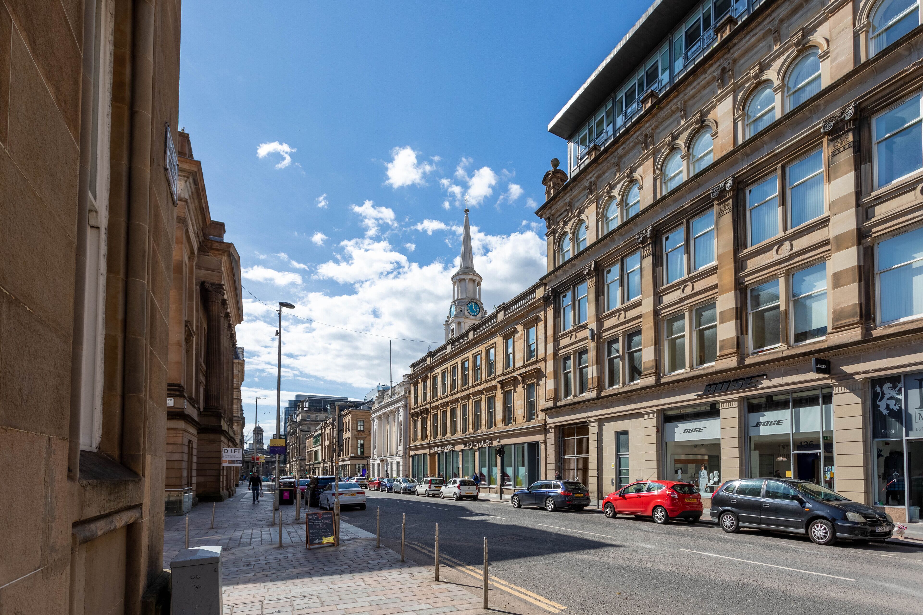 Une vue de rue avec des bâtiments historiques, une tour de l’horloge et des devantures de magasins, dont un magasin Bose.