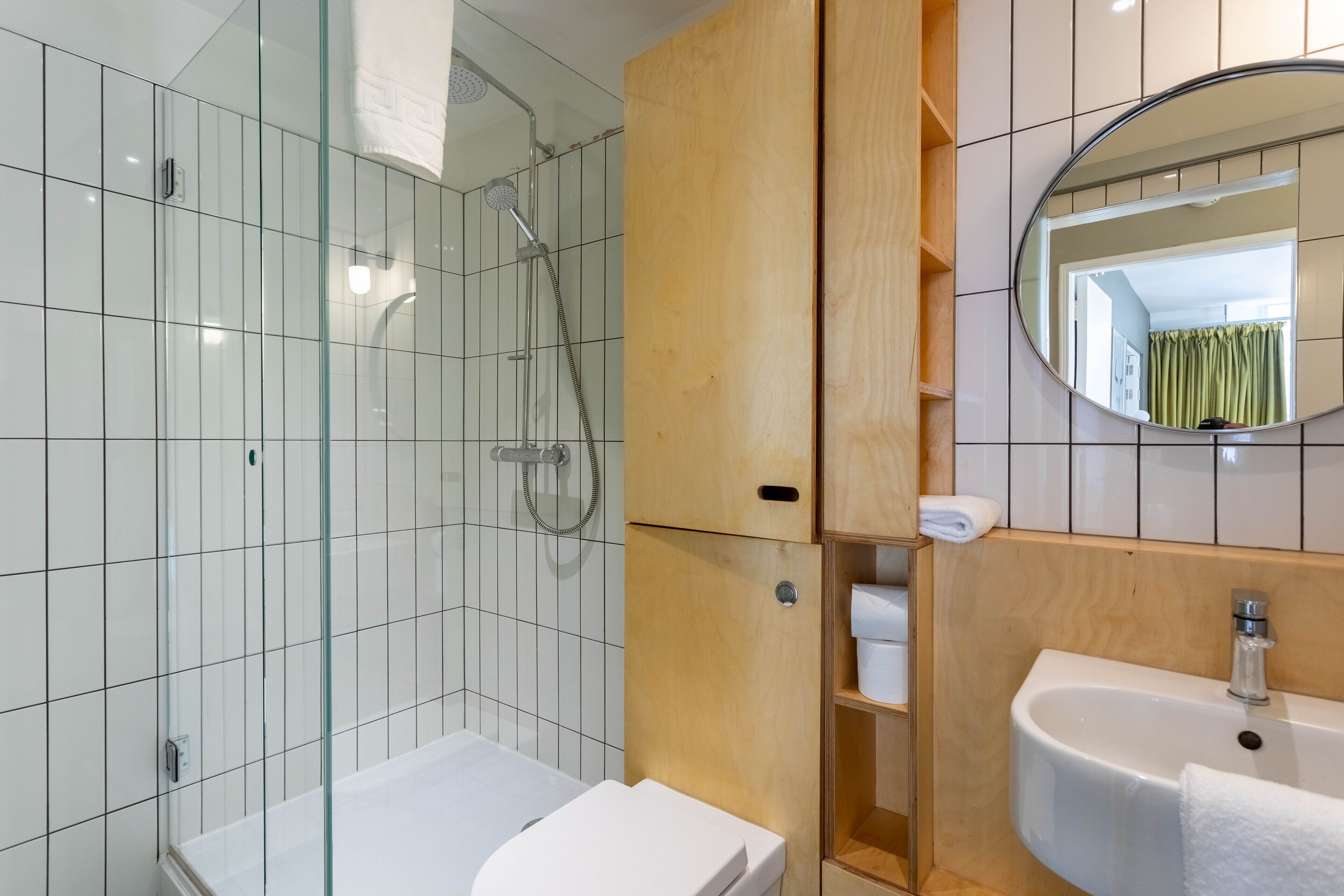 Un baño moderno con ducha envuelta en vidrio, un lavabo blanco y un mueble de tocador de madera.