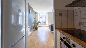 A modern kitchen with a Bosch refrigerator, wooden flooring, and a view to a living area through an open door. - Ingram Apartments (Glasgow)