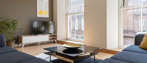 Un salon moderne avec un canapé, une table basse, un téléviseur et une grande fenêtre.