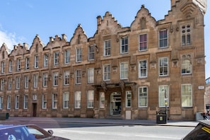 A row of historic stone buildings with uniform architectural style, large windows, and a central entrance. - Ingram Apartments (Glasgow)