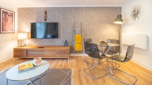 Un soggiorno moderno con televisore a schermo piatto, arredi in legno, un tavolo da pranzo in vetro e un elemento decorativo a parete.