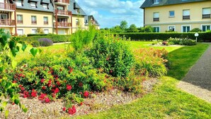 Ett hotell med flera våningar, en välskött trädgård med olika växter och blommor samt en klarblå himmel.