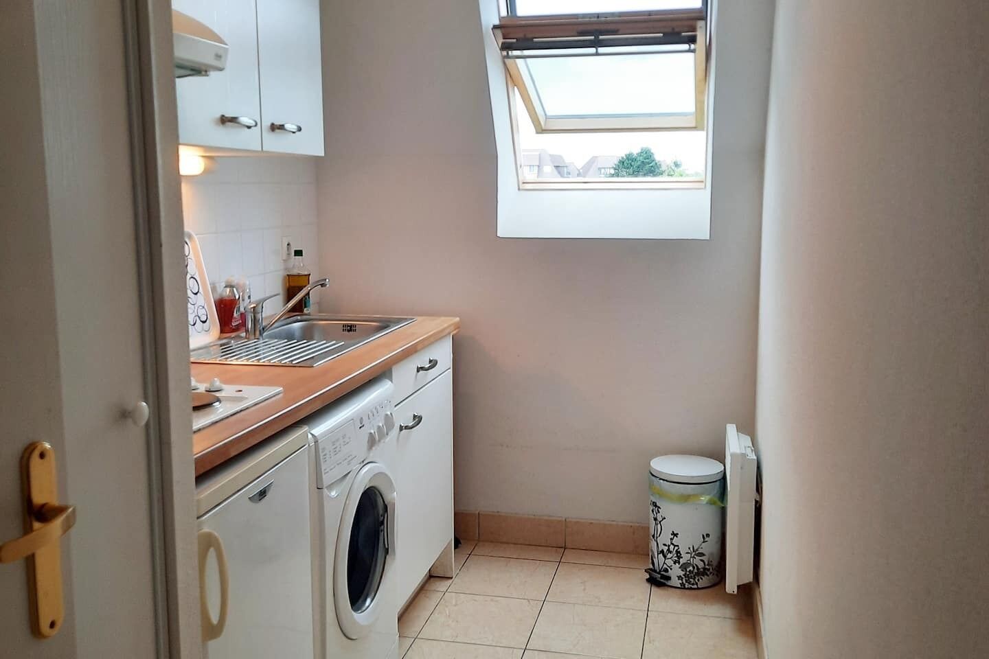 Une cuisine de taille réduite équipée d’un lave-linge, d’un évier et d’une fenêtre.