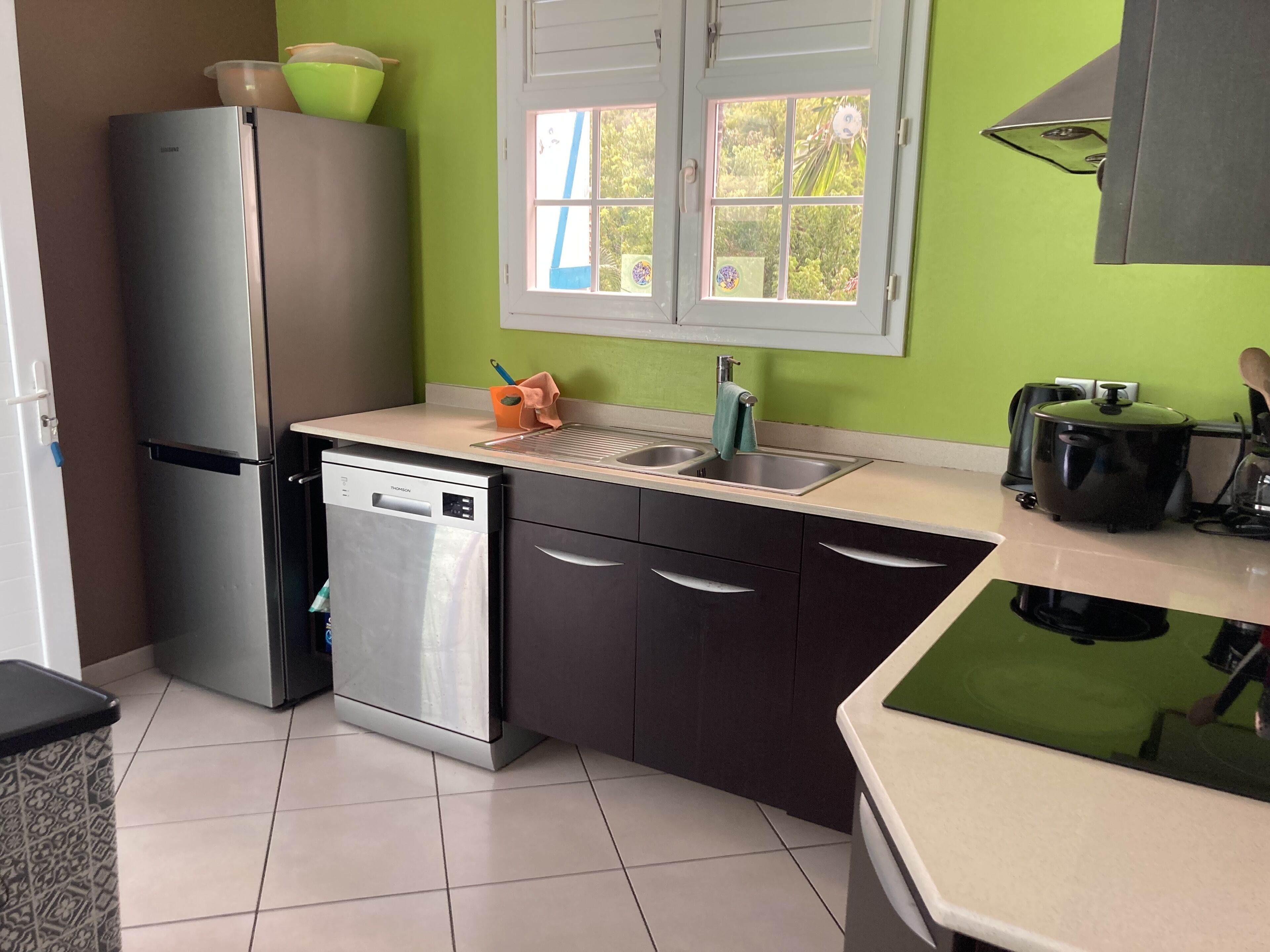Una cocina compacta equipada con lavavajillas, refrigerador, pileta y una ventana con persianas.