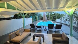 An outdoor patio area with a pool, lounge chairs, and a covered seating area. - Villa SAMA at Clos Samana (Le Diamant)