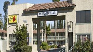 Entrada de un motel con un letrero sobre la puerta, un estacionamiento y un edificio con techo de tejas.